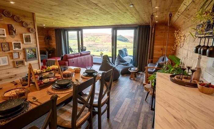 Open-plan living space features a lounge, swinging bench, fully equipped kitchen, and dining area with a wooden table for up to seven guests